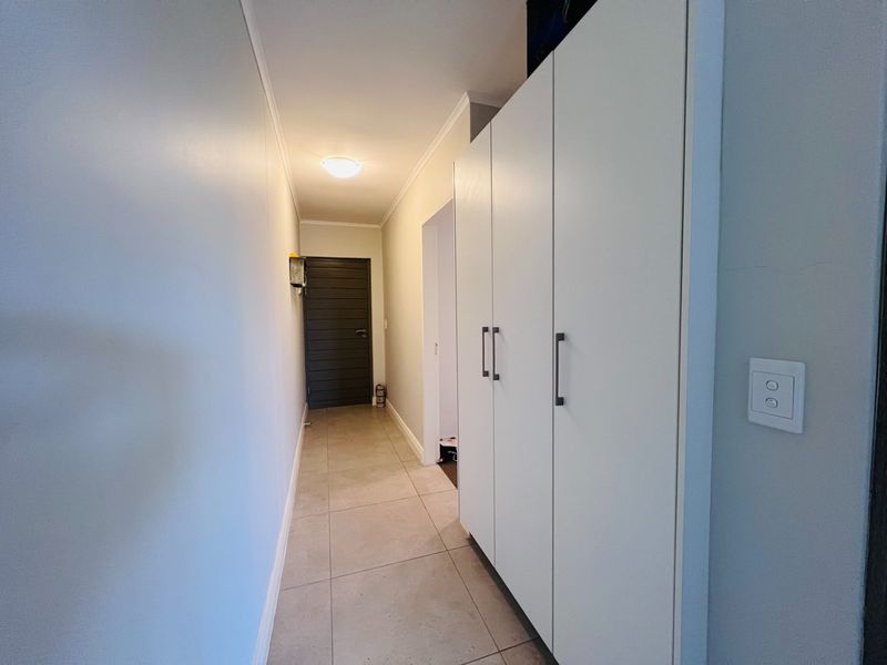 A clean and well-maintained hallway featuring neutral tiled flooring and ample built-in storage cupboards.