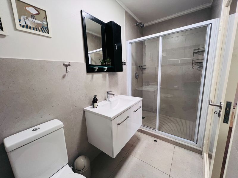 Modern bathroom featuring a wall-mounted vanity, a glass-enclosed shower with tiled finishes, and contemporary fixtures.