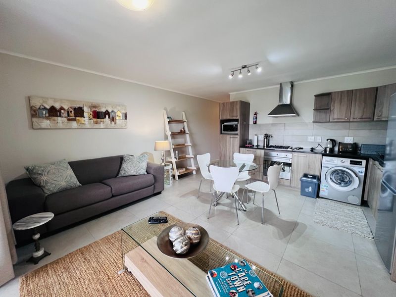 An open-plan living and kitchen area featuring tiled flooring, modern cabinetry, a gas hob, extractor fan, and integrated laundry plumbing.