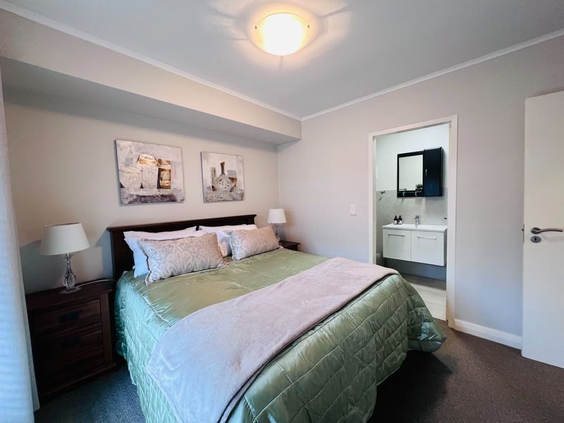 A well-maintained bedroom featuring neutral wall tones, carpeted flooring, and an adjoining en-suite bathroom with a modern vanity unit.
