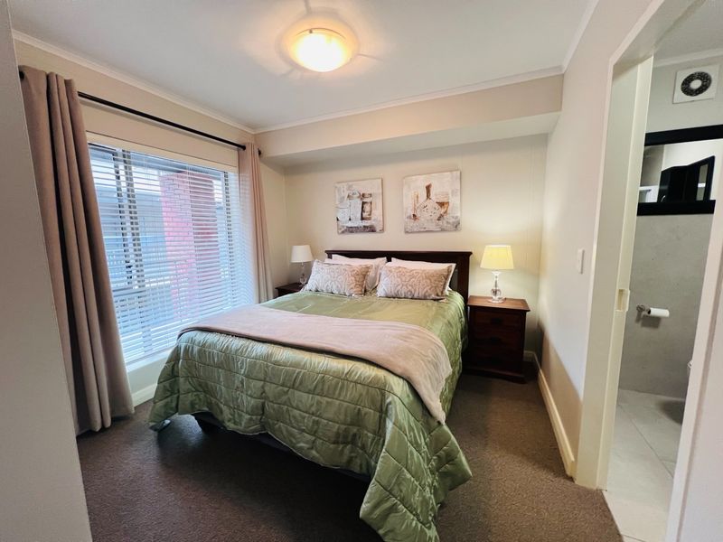 A well-lit bedroom featuring neutral walls, carpeted flooring, and a window with venetian blinds, offering a comfortable and functional living space.