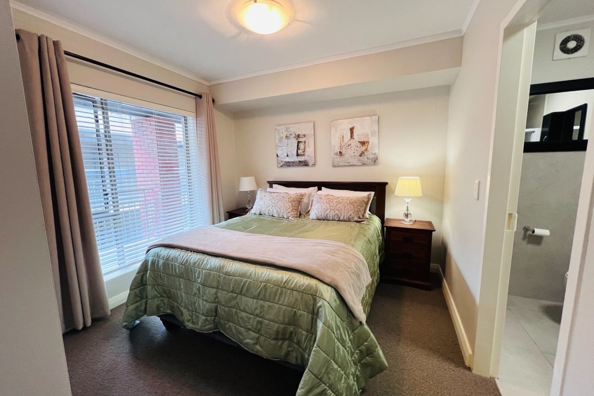A well-lit bedroom featuring neutral walls, carpeted flooring, and a window with venetian blinds, offering a comfortable and functional living space.