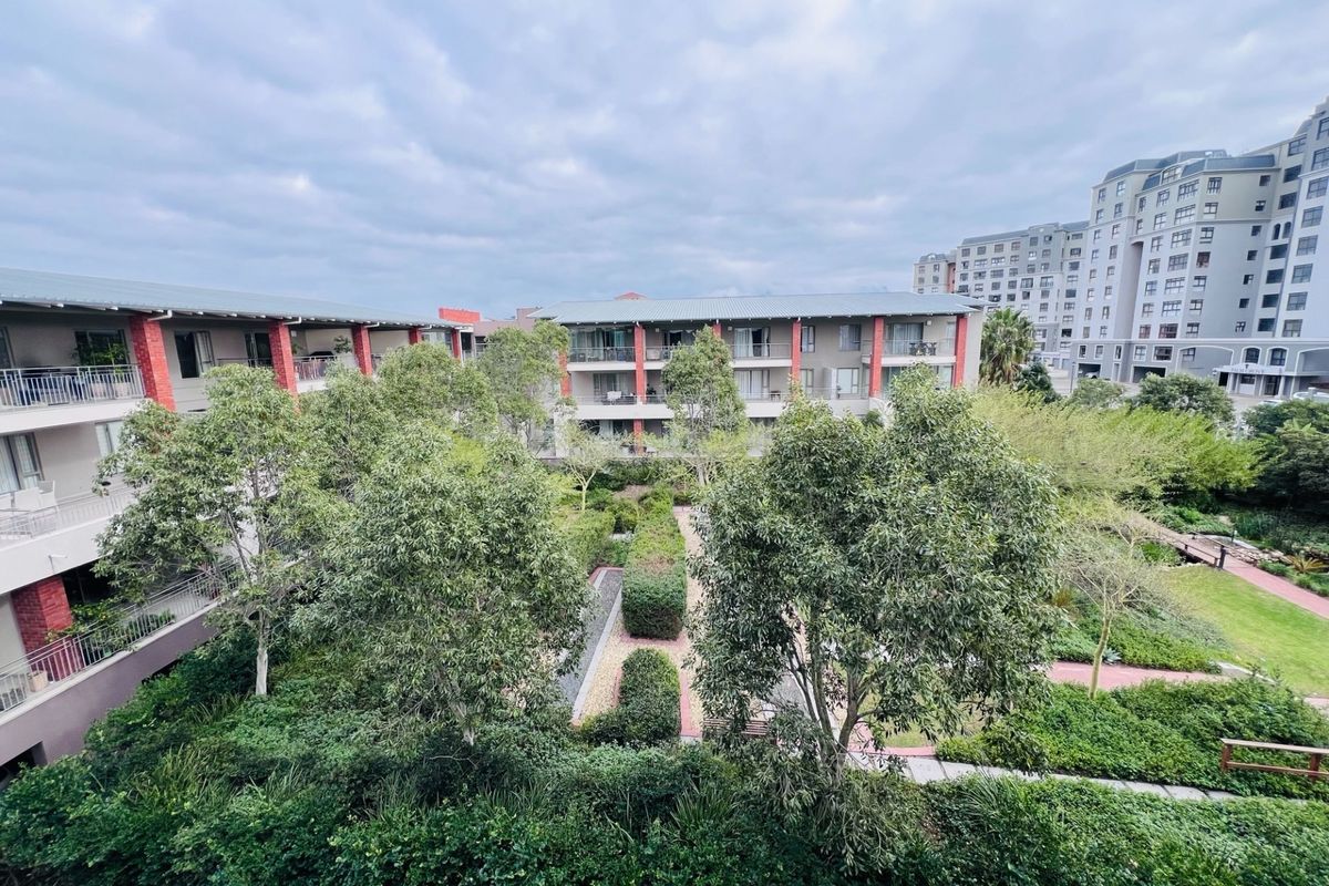 An elevated view of a well-maintained communal garden area surrounded by apartment blocks with private balconies and landscaped pathways.