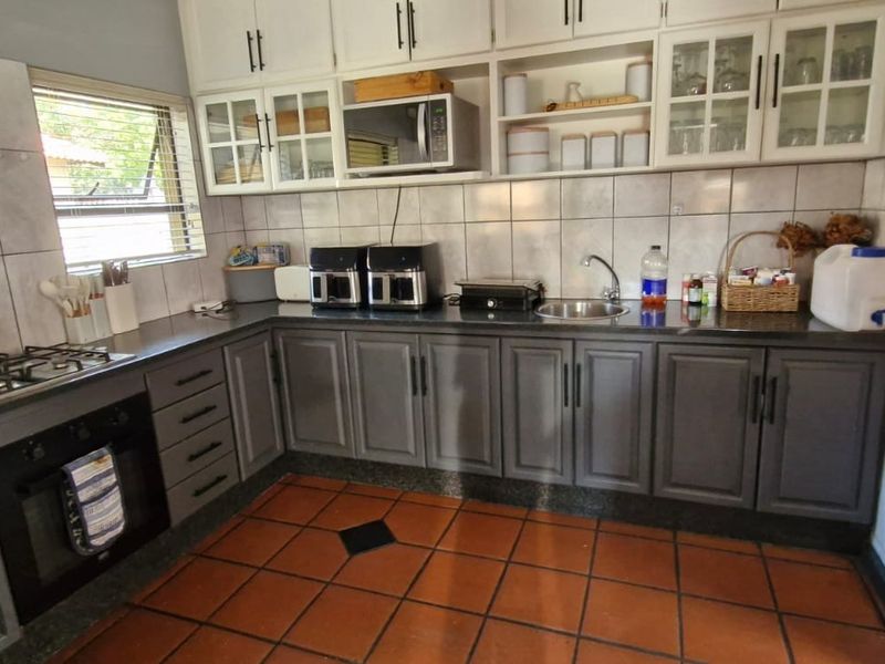 A functional kitchen featuring grey lower cabinetry, white upper cabinets, tiled splashbacks, a gas hob, and a built-in oven with terracotta floor tiles.
