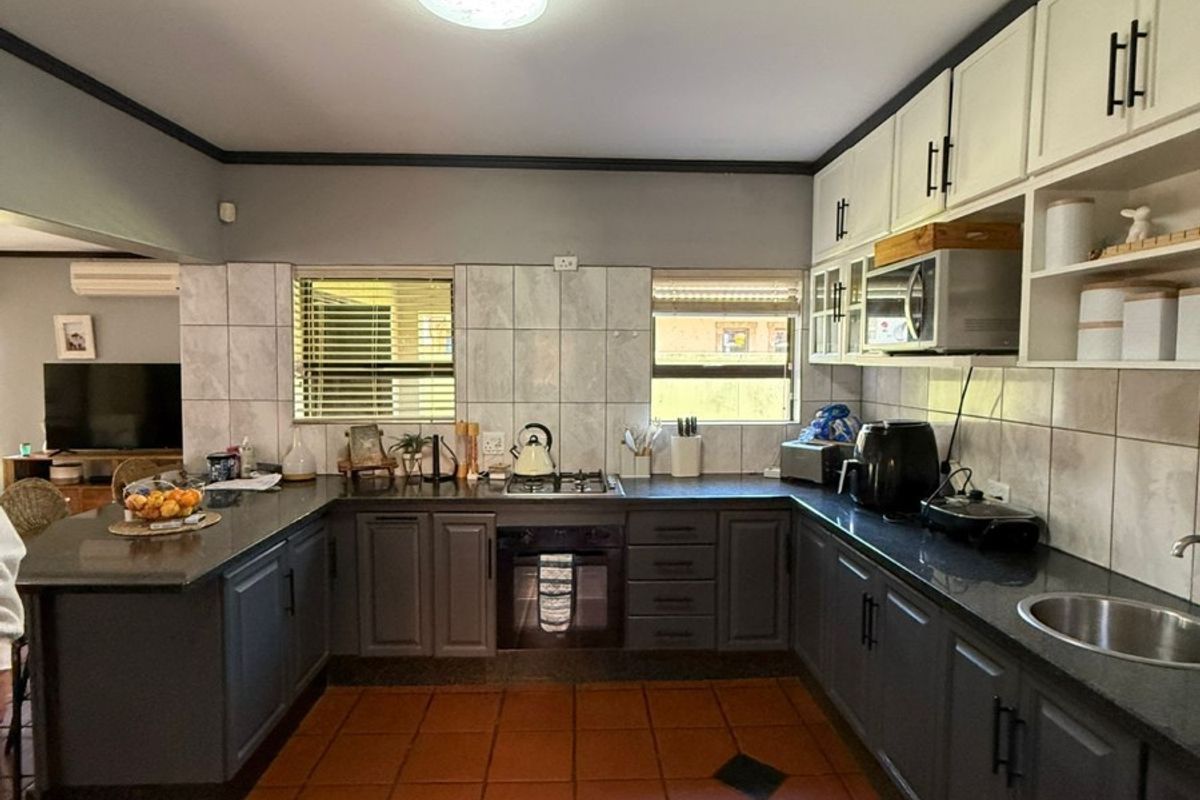 A functional kitchen featuring dark grey lower cabinetry, contrasting white upper cabinets, granite countertops, a gas hob, and durable terracotta floor tiles.