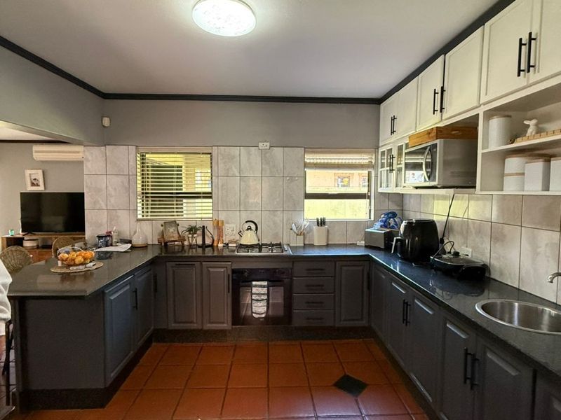 A functional kitchen featuring dark grey lower cabinetry, contrasting white upper cabinets, granite countertops, a gas hob, and durable terracotta floor tiles.