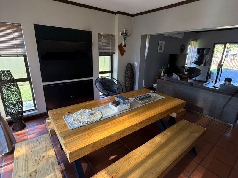 Spacious open-plan living and dining area featuring terracotta tiled flooring, built-in media cabinetry, and direct access to the outdoor patio through sliding glass doors.