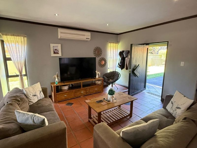 A comfortable living room featuring terracotta floor tiles, recessed downlighting, and a wall-mounted split-system air conditioner, with direct access to the outdoor area.