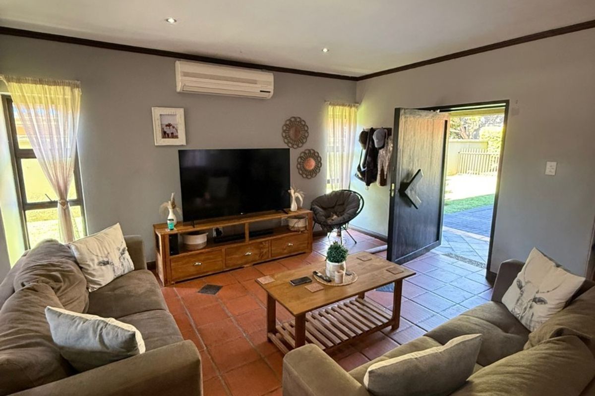 A comfortable living room featuring terracotta floor tiles, recessed downlighting, and a wall-mounted split-system air conditioner, with direct access to the outdoor area.