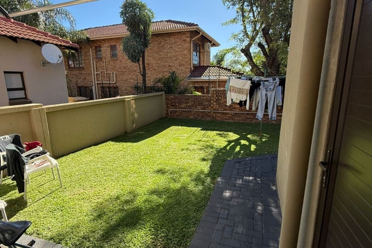 A private rear garden featuring a well-maintained lawn, paved walkway, and a protective polycarbonate awning over the access area.