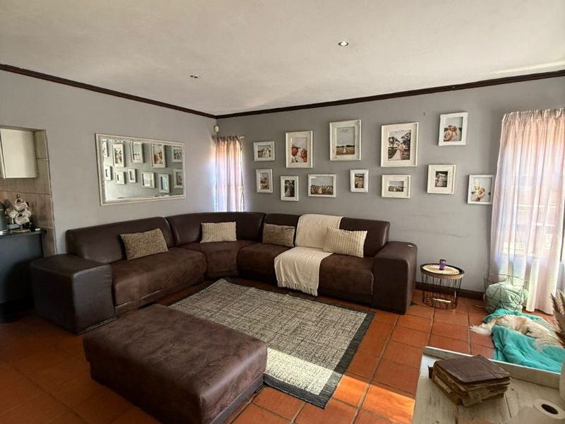 A spacious living room featuring traditional terracotta floor tiles, neutral grey walls, and recessed ceiling lighting, offering a comfortable and functional family living space.