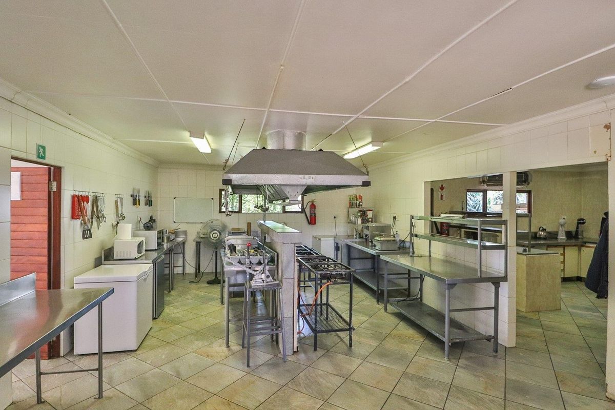 A functional commercial-style kitchen featuring stainless steel prep surfaces, a central extractor hood, and durable tiled finishes throughout the workspace.