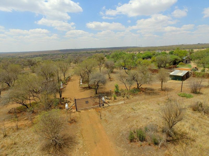 Aerial view of a rural farm property featuring a gated entrance, dirt driveway, and surrounding natural landscape with outbuildings.