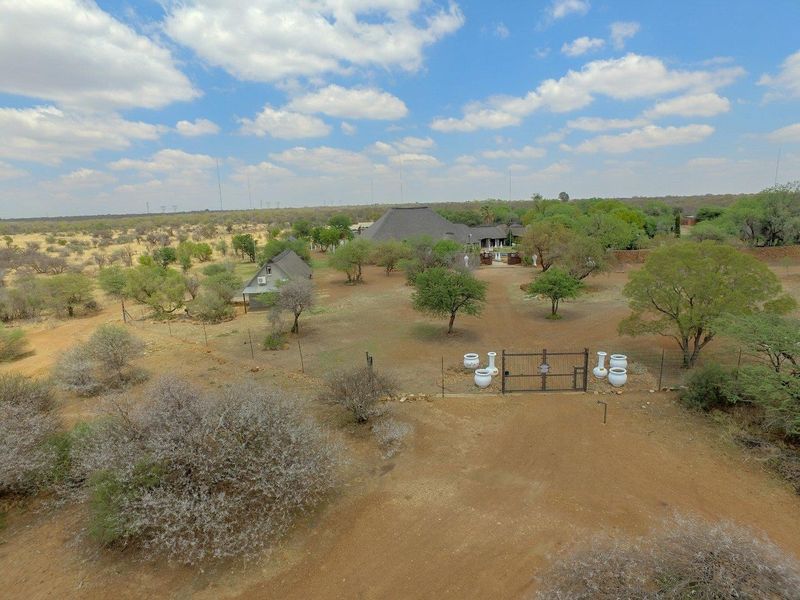 Aerial view of a rural farm property featuring multiple thatched-roof buildings, a gated entrance, and expansive natural landscape.