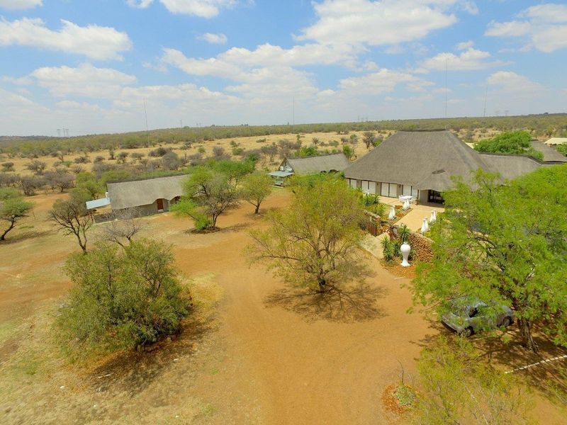 Aerial view of a farm property featuring multiple buildings with traditional thatch roofs, a paved patio area, and expansive surrounding landscape.