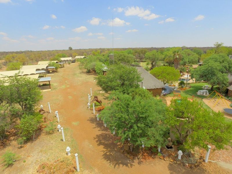 Aerial view of the farm property featuring a thatched roof building, swimming pool, landscaped gardens, and multiple outdoor structures set in a rural landscape.
