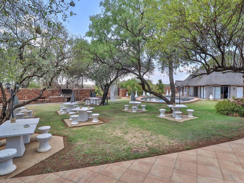Spacious outdoor entertainment area featuring a swimming pool, built-in braai, stone walling, and mature trees set within a landscaped garden.