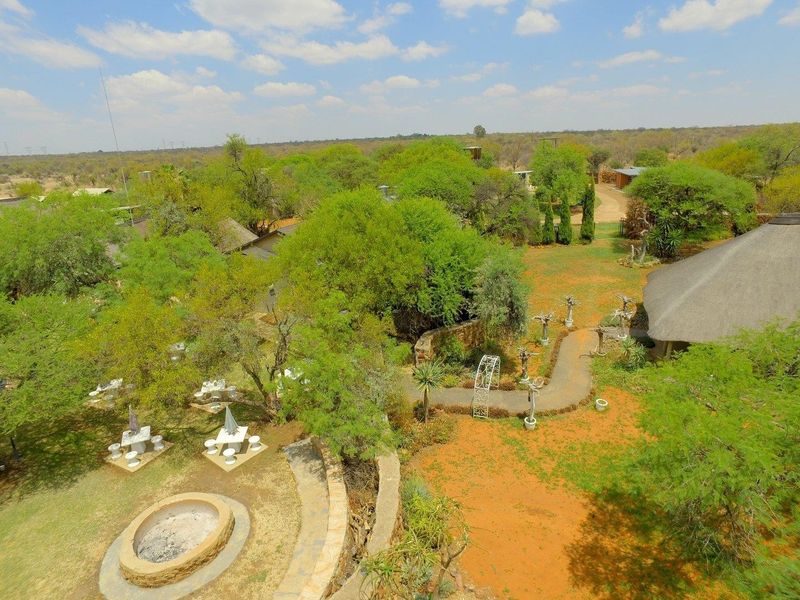Aerial view of a farm property featuring a thatched roof building, landscaped garden areas, paved pathways, and a stone-encased fire pit.