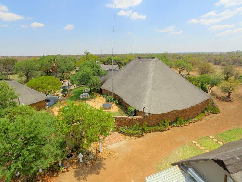Aerial view of a farm property featuring a large thatched-roof building with stone walls, surrounded by mature trees and landscaped garden areas.