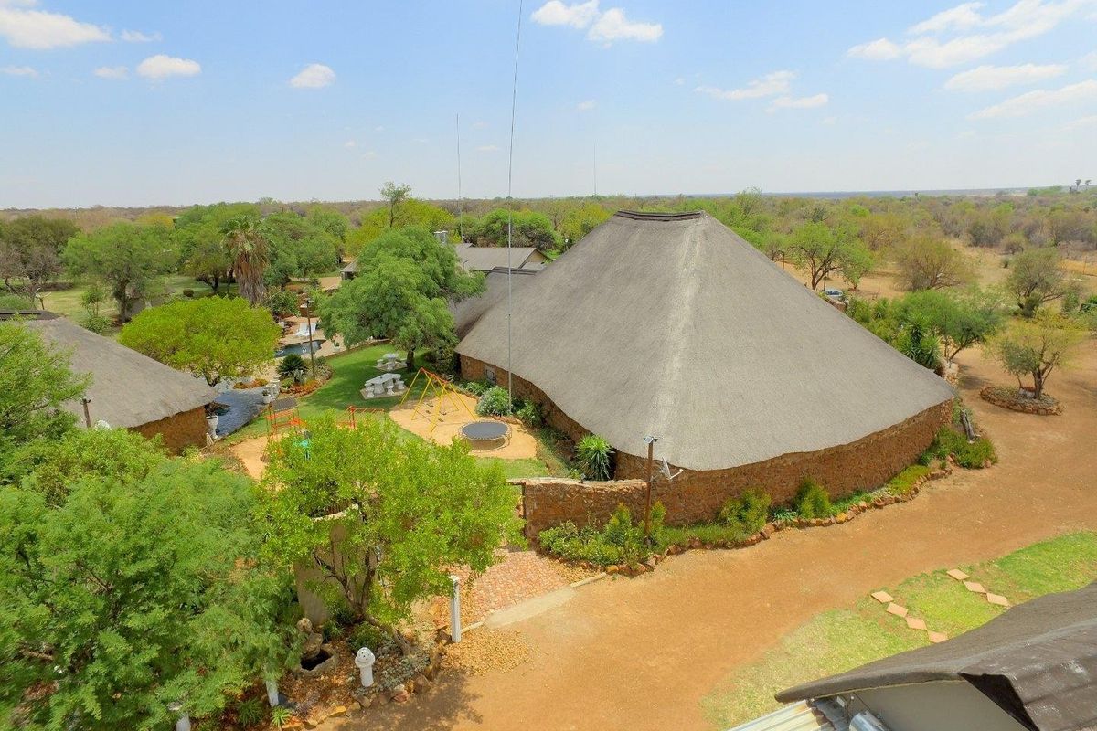 Aerial view of a farm property featuring a large thatched-roof building with stone walls, surrounded by mature trees and landscaped garden areas.