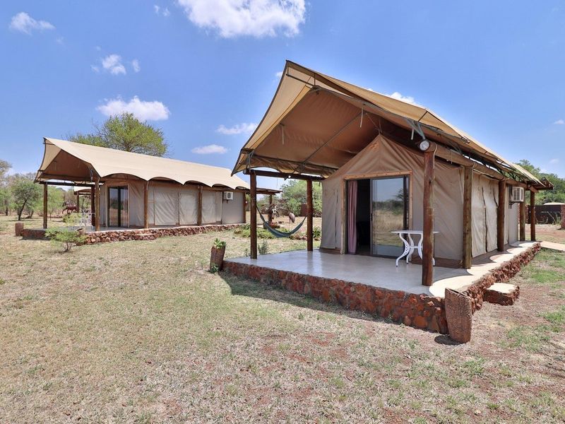 Two luxury safari-style tented units featuring stone foundations, tiled patios, and sliding glass door entrances set within a natural farm landscape.