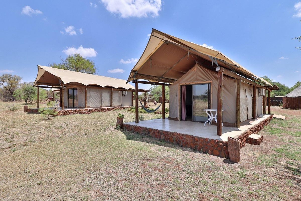 Two luxury safari-style tented units featuring stone foundations, tiled patios, and sliding glass door entrances set within a natural farm landscape.