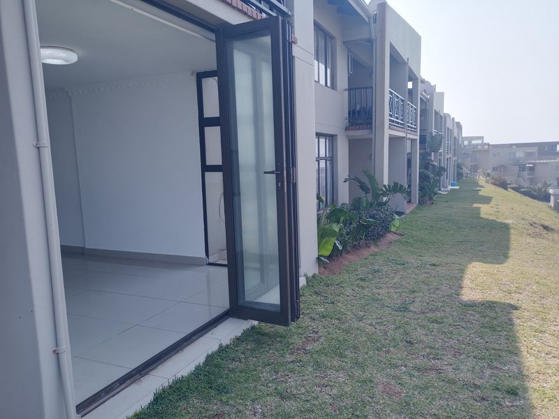 Rear view of the apartment complex featuring bi-fold glass doors opening onto a shared lawn area with balcony access above.