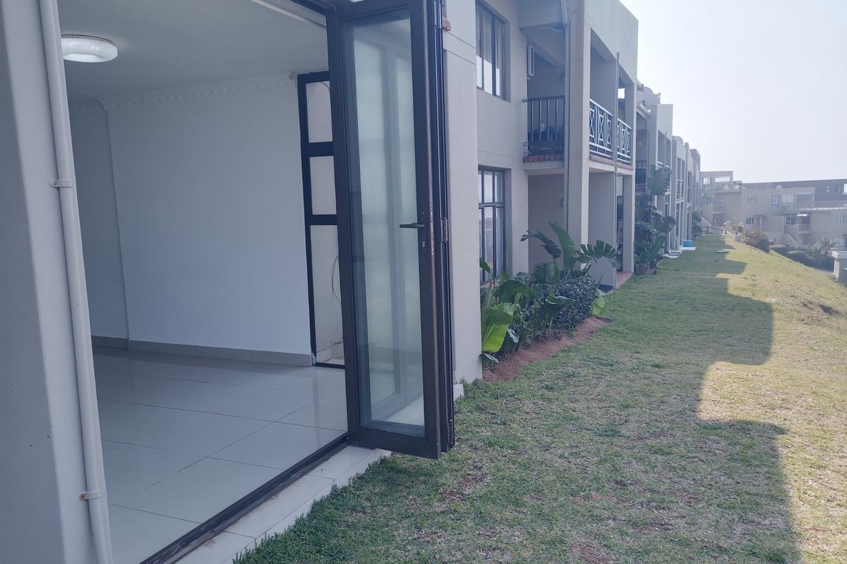Rear view of the apartment complex featuring bi-fold glass doors opening onto a shared lawn area with balcony access above.