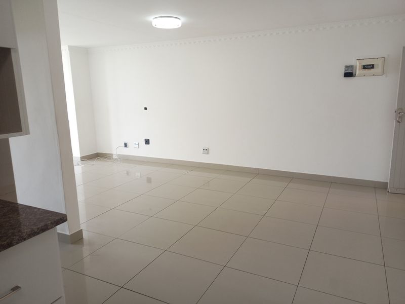 A bright, empty open-plan living area featuring neutral tiled flooring, clean white walls, and modern electrical fixtures, ready for personalization.