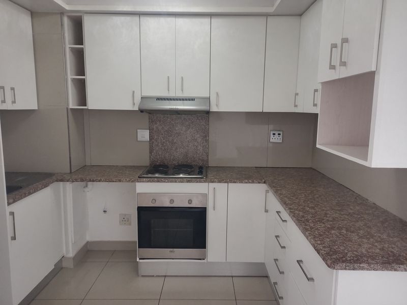 A functional kitchen featuring white cabinetry, laminate countertops, a built-in oven, and an electric hob, offering a clean and practical workspace.