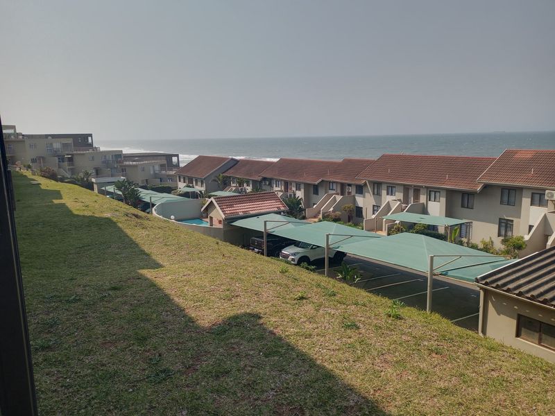 Elevated coastal view overlooking the apartment complex, featuring tiled roofs, covered parking bays, a swimming pool, and well-maintained lawn areas.