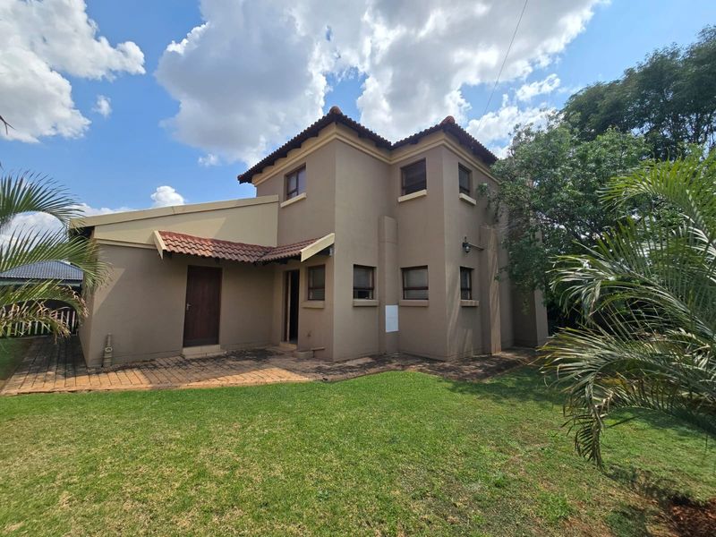 Rear view of a two-story house featuring a paved patio area, plastered exterior walls, and a tiled roof set within a garden.