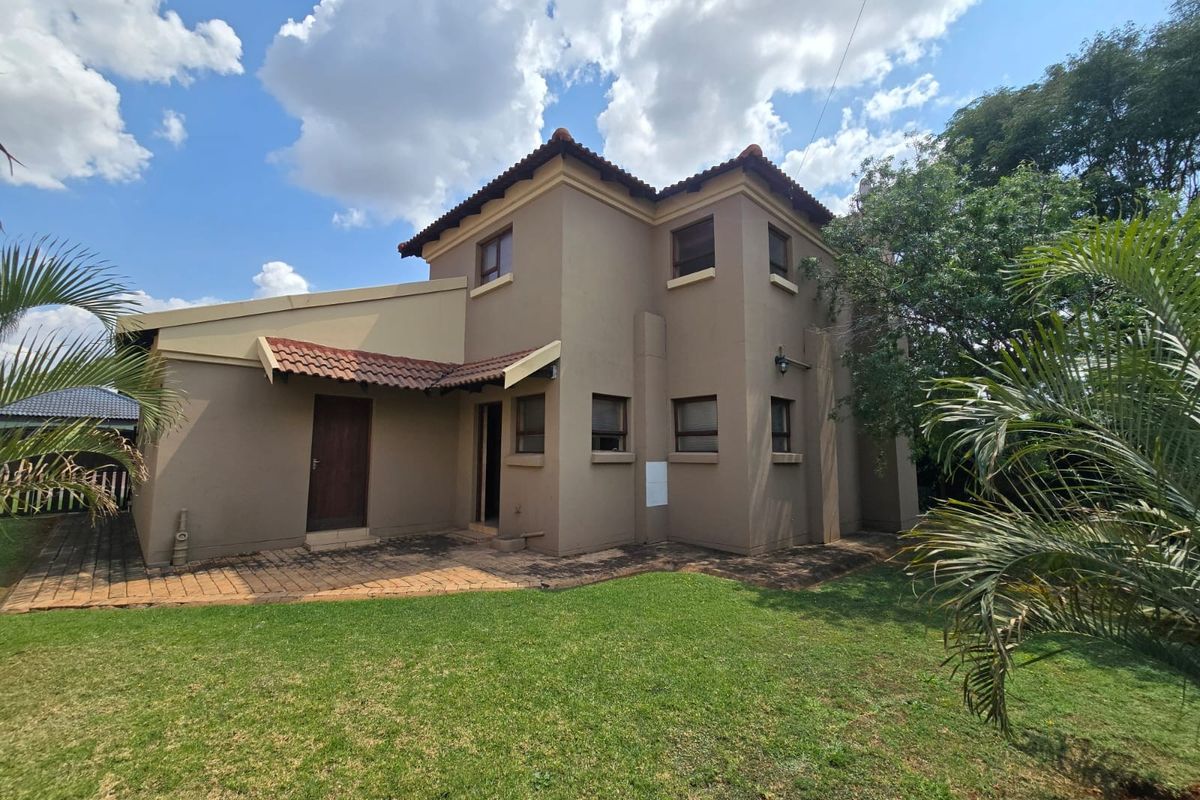 Rear view of a two-story house featuring a paved patio area, plastered exterior walls, and a tiled roof set within a garden.