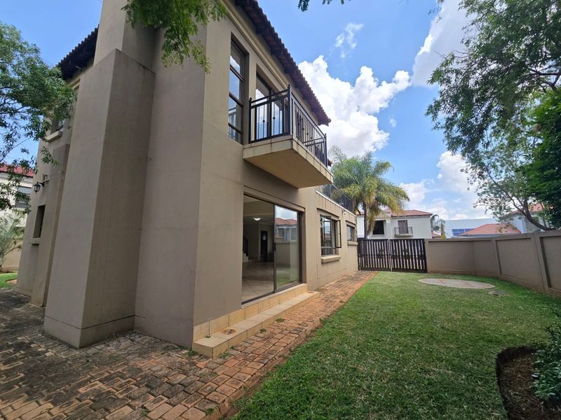 Rear view of the property featuring a private garden, paved patio area, and an upper-level balcony with metal railings.