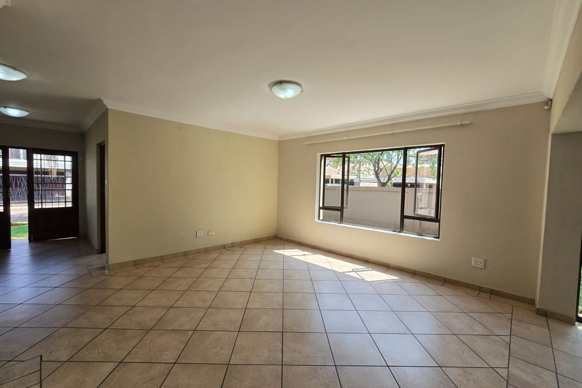 A spacious, empty living area featuring neutral tiled flooring, coved cornicing, and large aluminium-framed windows allowing for natural light.