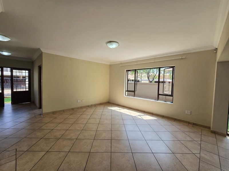 A spacious, empty living area featuring neutral tiled flooring, coved cornicing, and large aluminium-framed windows allowing for natural light.