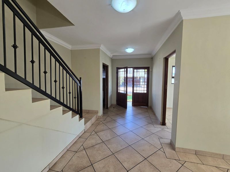 Spacious entrance hall featuring tiled flooring, a wrought iron staircase railing, and a timber-framed glass front door leading to the exterior.