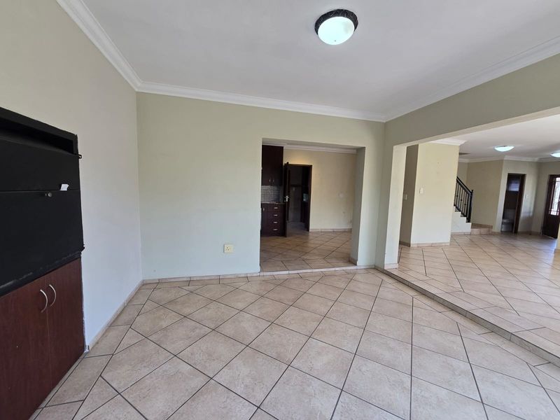 Spacious open-plan living area featuring neutral tiled flooring, built-in cabinetry, and a split-level layout leading to a staircase and additional rooms.