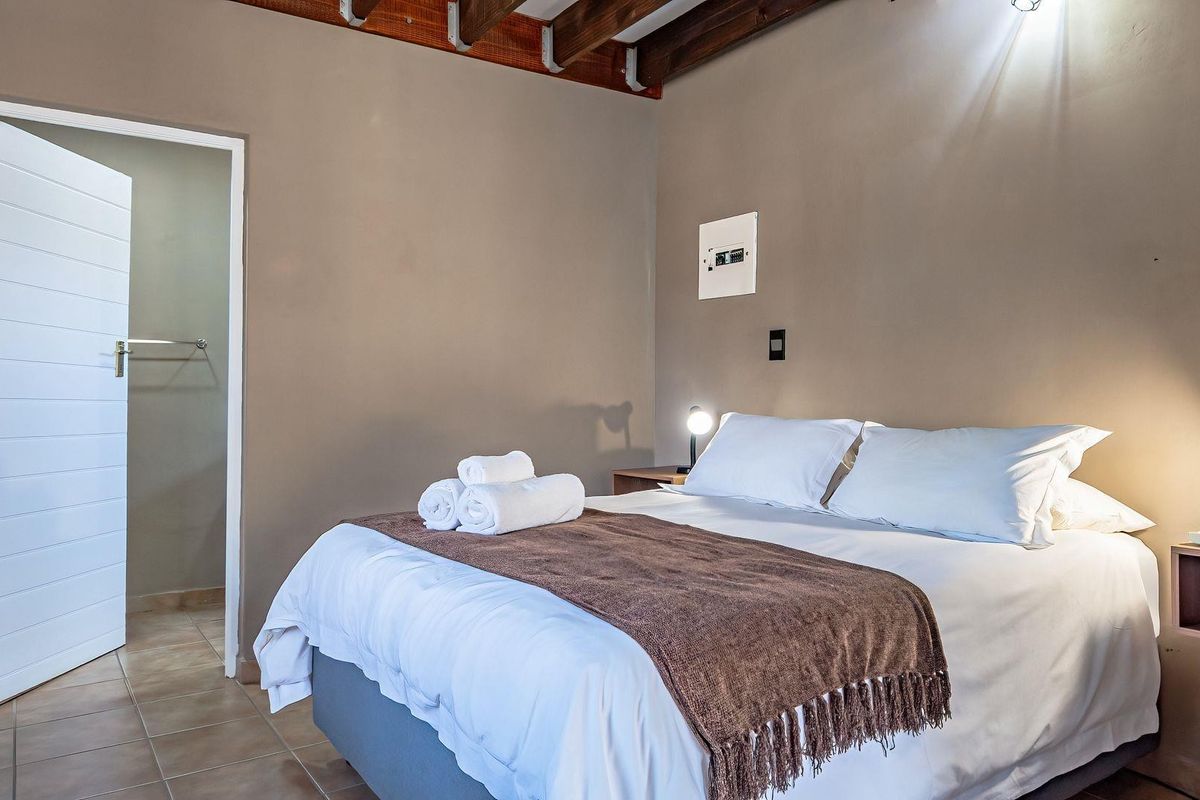 A cozy bedroom featuring exposed timber ceiling beams, tiled flooring, and an en-suite access door.