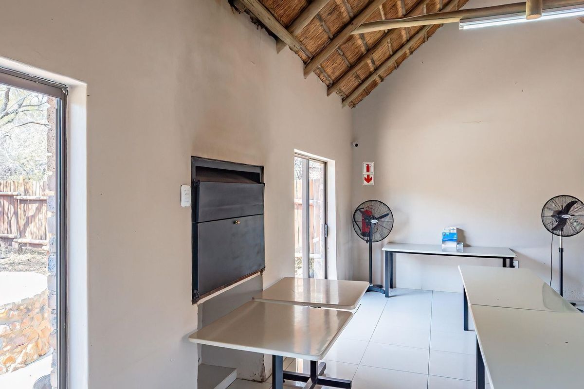 Spacious living area featuring a traditional thatched roof with exposed rafters, tiled flooring, built-in fireplace, and direct access to the garden through sliding doors.