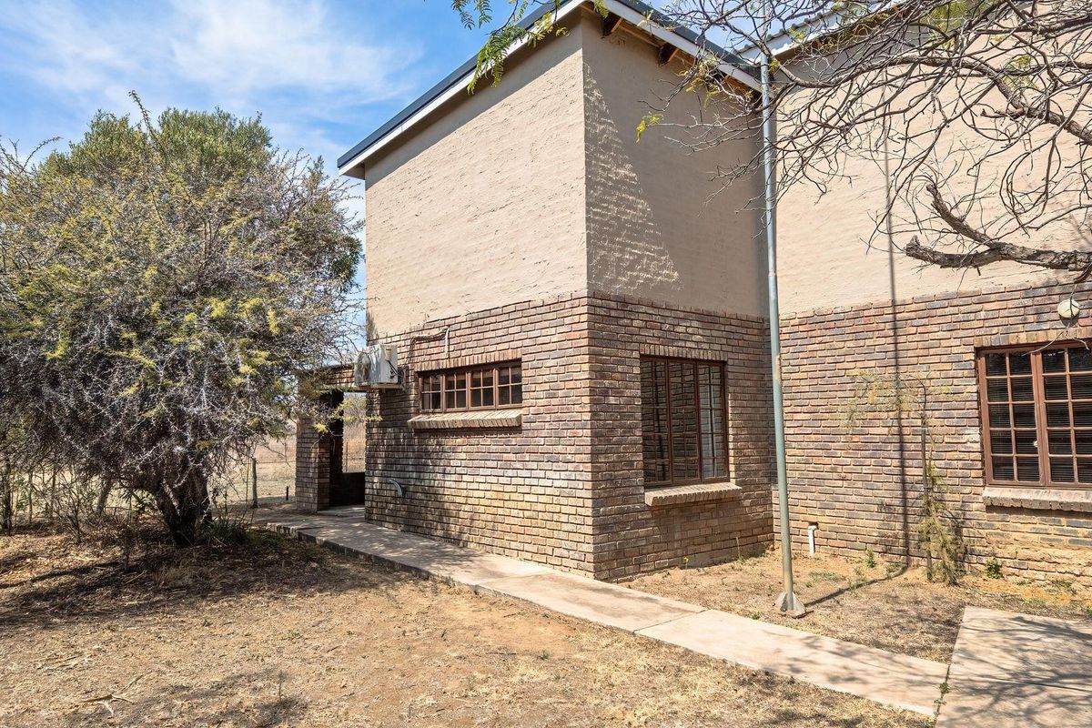 Rear view of a two-story farm building featuring a combination of face brick and plastered walls with a concrete pathway.