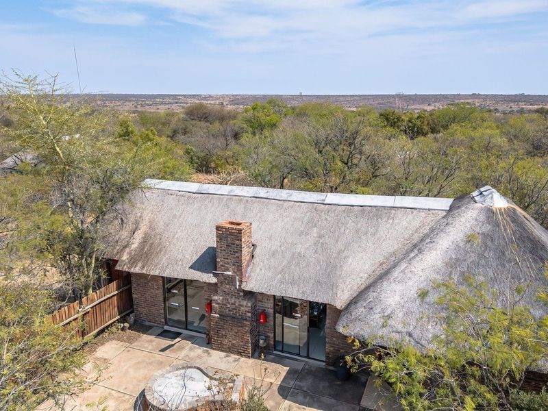 Aerial view of a farm-style dwelling featuring a traditional thatch roof, brick chimney, and an outdoor concrete patio area with a fire pit.