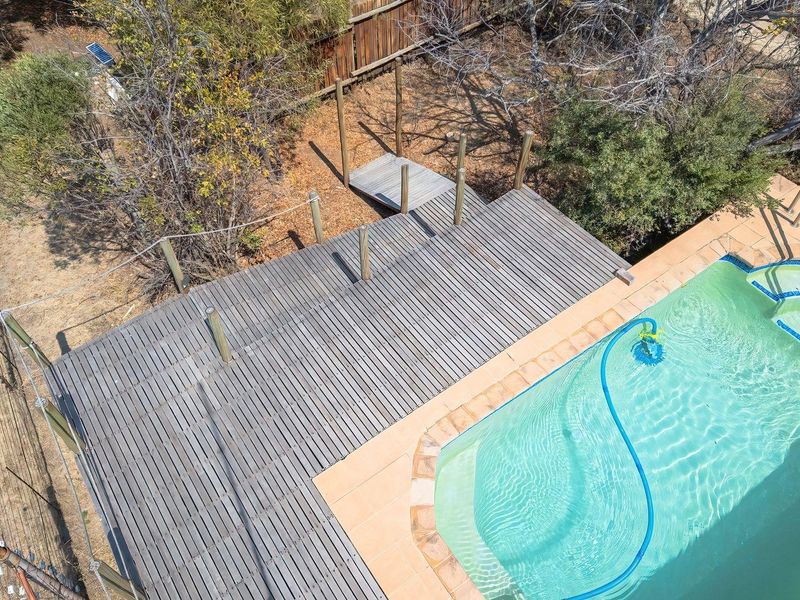 Aerial view of a swimming pool area featuring a timber deck, tiled pool surround, and integrated steps, set within a natural garden landscape.