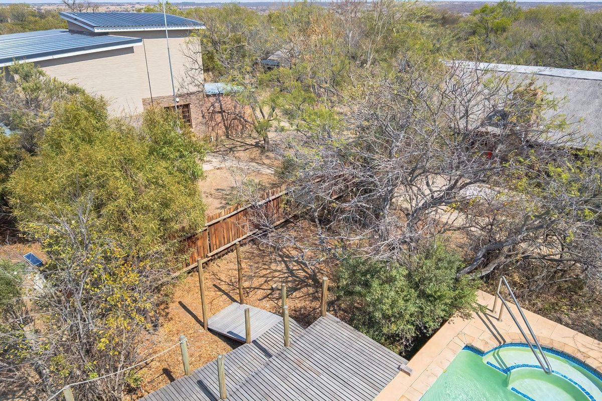 Aerial view of the property grounds featuring a swimming pool, timber decking, and a mix of modern and traditional thatched roof structures.