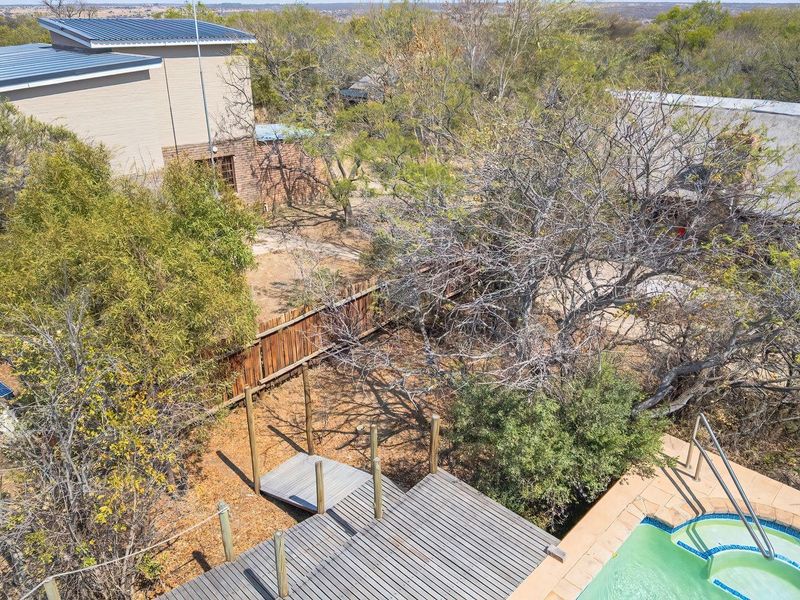 Aerial view of the property grounds featuring a swimming pool, timber decking, and a mix of modern and traditional thatched roof structures.