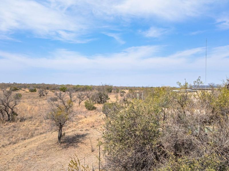 A wide-angle view of the expansive, arid farm landscape featuring native scrub vegetation and open fields under a clear blue sky.