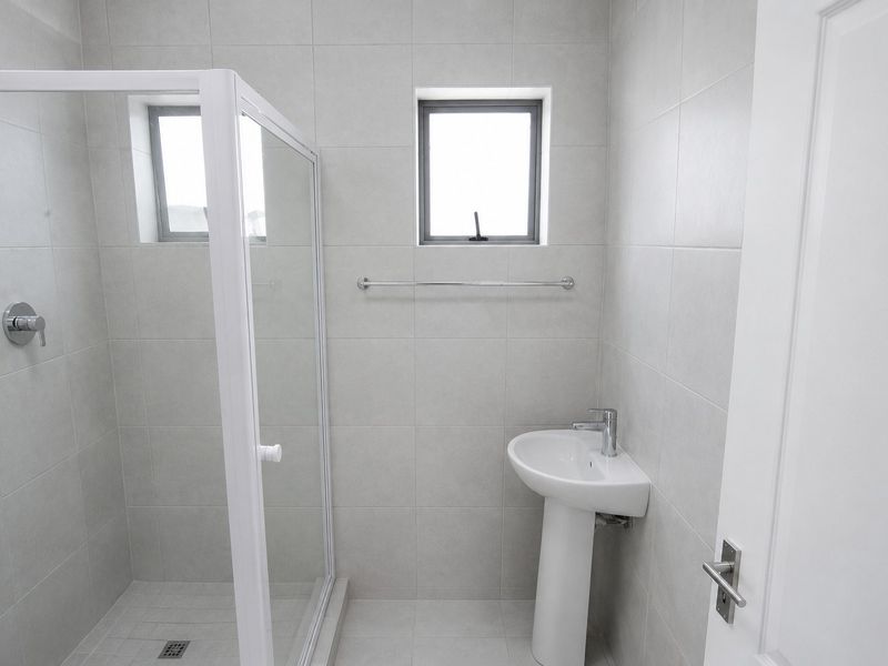 A clean, modern bathroom featuring a glass shower enclosure, pedestal basin, and neutral wall tiling.