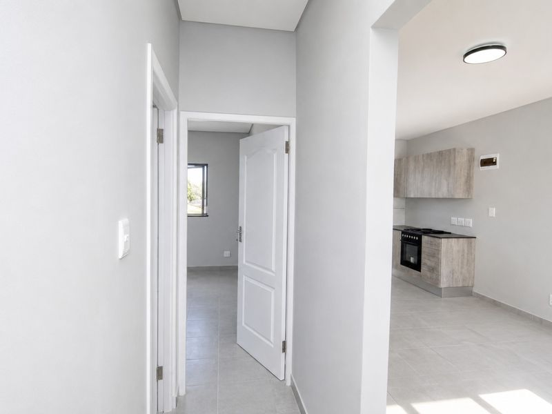 A bright, modern hallway leading into an open-plan kitchen area featuring neutral finishes, tiled floors, and contemporary cabinetry with integrated appliances.