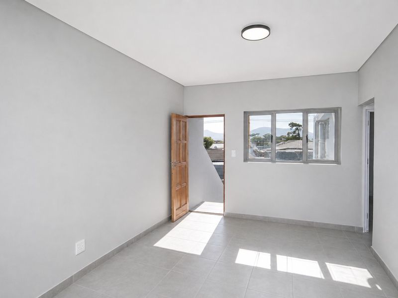 A bright, empty bedroom featuring neutral grey walls, tiled flooring, and a timber door leading to an outdoor area.