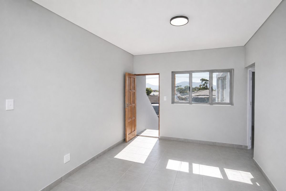 A bright, empty bedroom featuring neutral grey walls, tiled flooring, and a timber door leading to an outdoor area.